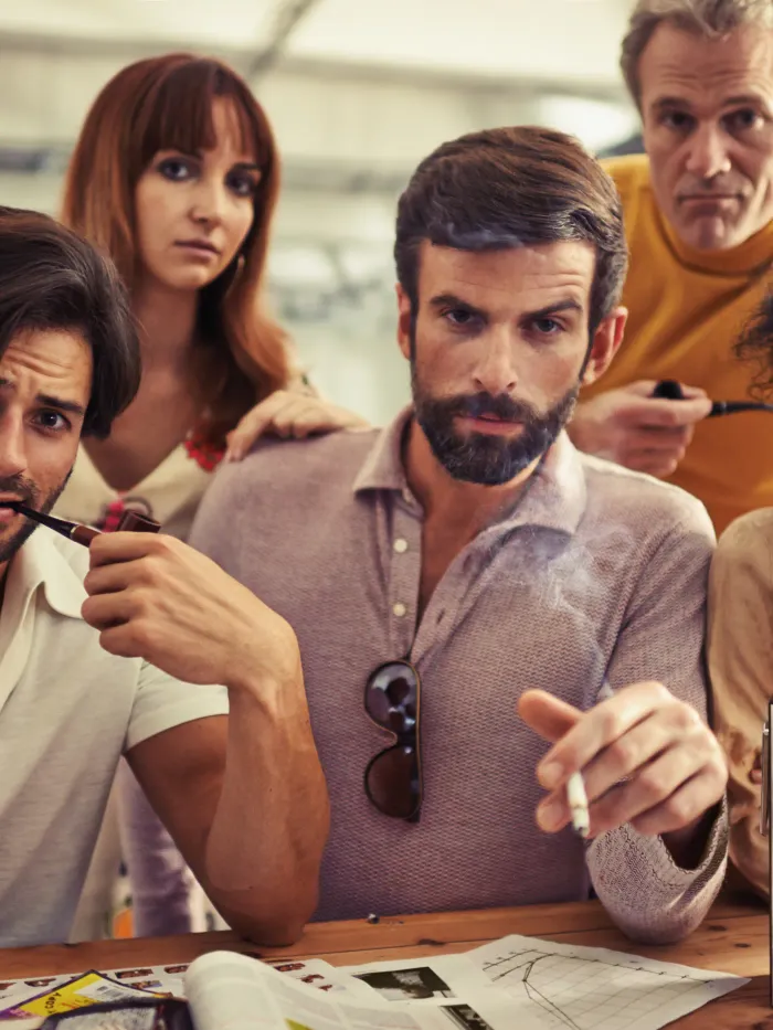 Groupe de personnes au travail dans les années 70 avec des cigarettes et pipes